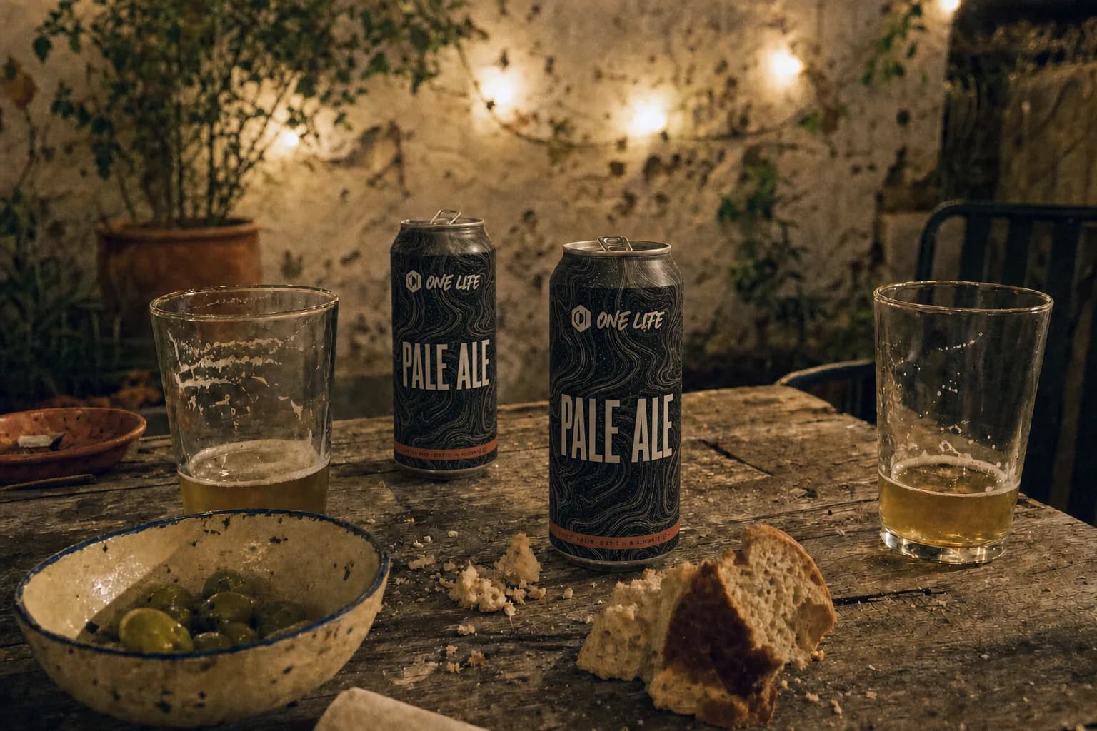 Render of a shared night table under string lights with two One Life Pale Ale cans, bread and olives